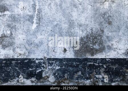Old white painted concrete wall with dark baseboard, grunge background or texture Stock Photo