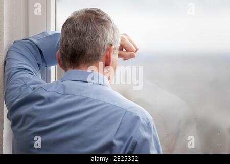 Tired or sorrowful businessman looking out of a window - focus on the hand and the window Stock Photo