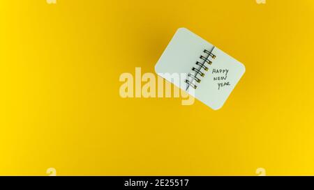 Overhead shot of a small notebook with Happy New Year text on it on a yellow background Stock Photo