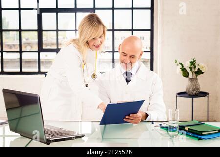 Shot of male doctor sitting at desk while female doctor standing next to him and consulting. Group of medical team working together in the doctor’s of Stock Photo