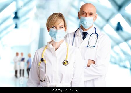Shot of female and male doctors wearing face masks and standing together on the clinic’s foyer while looking at camera. Medical team. Doctors wearing Stock Photo