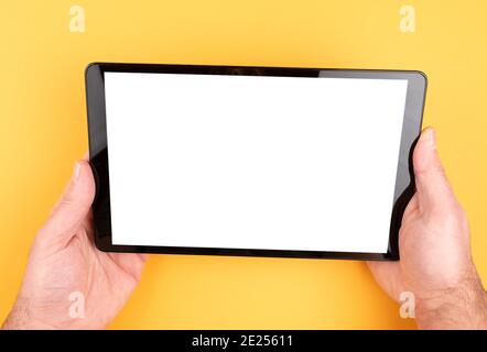 close-up view of hands holding tablet computer with copy space on screen against orange colored background Stock Photo