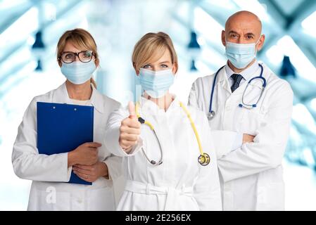 Shot of female and male doctors standing together on the clinic’s foyer while female doctor giving thumbs up. Medical team. Doctors wearing face masks Stock Photo