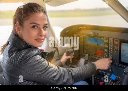 Beautiful Smiling Woman Pilot Sitting in Cabin of Modern Aircraft. Portrait of Female Pilot in the Light Aircraft Cockpit. Stock Photo