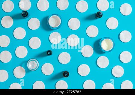 Hygiene products: white round cotton pads and plastic sticks for cleaning the ears lie on a blue background next to face cream. Top view, flat lay Stock Photo