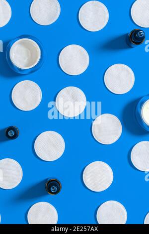 Hygiene products: white round cotton pads and plastic sticks for cleaning the ears lie on a blue background next to face cream. Top view, flat lay Stock Photo