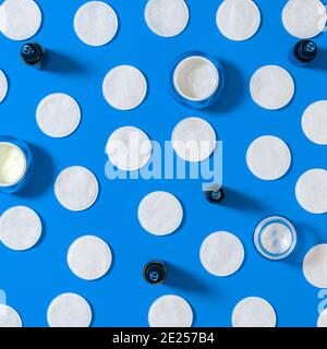 Hygiene products: white round cotton pads and plastic sticks for cleaning the ears lie on a blue background next to face cream. Top view, flat lay Stock Photo