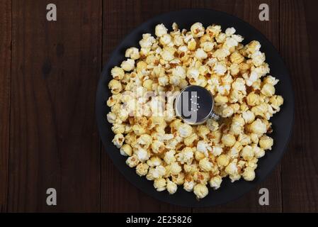 Overhead shot of a salt shaker in a shallow bowl surrounded by fresh made popcorn. Horizontal format on rustic dark table with copy space. Stock Photo