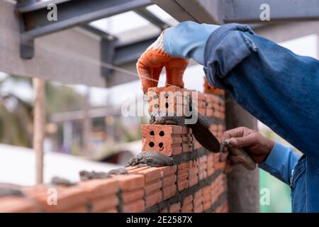 Bricklayer worker installing brick masonry exterior wall with trowel putty knife on construction site Stock Photo