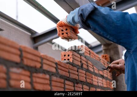 Close up hand of Bricklayer worker installing brick masonry on exterior wall on construction site Stock Photo