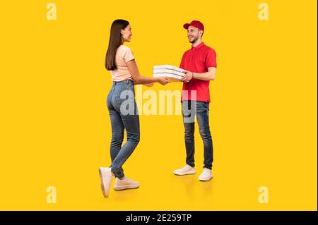 Courier Guy Giving Pizza Boxes To Lady On Yellow Background Stock Photo