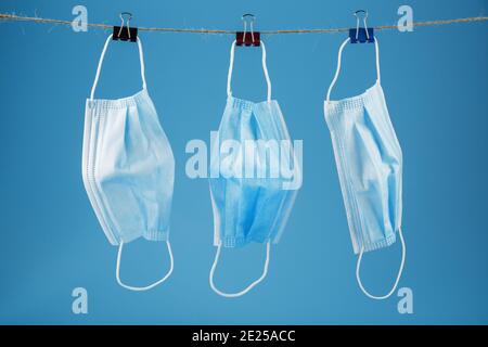 Three surgical masks hang on a clothesline against a blue background. Free space Stock Photo
