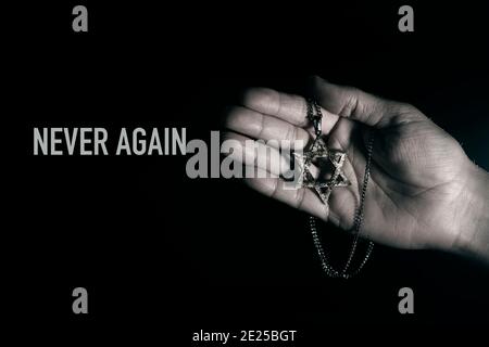 closeup of an old and rusty pendant in the shape of the star of david on the hand of a man and the text never again, in reference to the holocaust Stock Photo