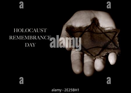 closeup of the star of david in an old and ragged badge on the hand of a man, and the text holocaust remembrance day on a black background Stock Photo