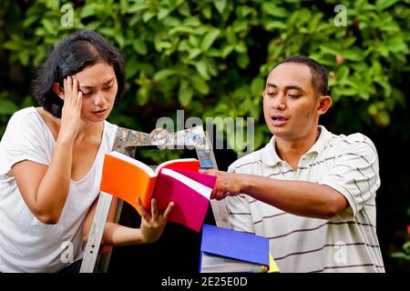 Southeast Asian ethnic young man and woman sitting on a ladder studying together and having discussion over books Stock Photo