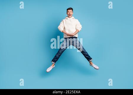 Photo portrait full body view of funny guy jumping up spreading legs like star wearing woolen hoodie isolated on pastel blue colored background Stock Photo