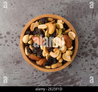Top view of an assortment of nuts and dried fruit in a wood bowl atop a gray background. Stock Photo