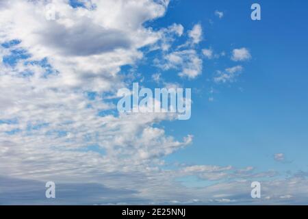 White fluffy clouds spread across the sky, revealing pure blue and splitting the picture in half. Stock Photo