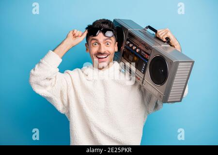 Photo portrait of excited man with stubble lifting up glasses holding boombox on shoulder isolated on pastel blue colored background Stock Photo