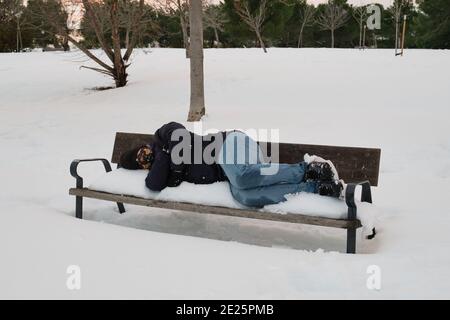 Unrecognizable homeless man sleeping on bench in snowy cold winter. Filomena snowstorm in Madrid, Spain. Stock Photo
