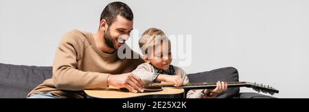 happy man teaching son playing acoustic guitar isolated on grey, banner Stock Photo