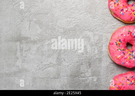 Border of three pink donuts doughnuts with sprinkles on a grey concrete surface with copy space and room for text Stock Photo