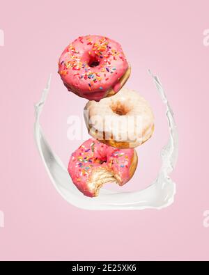 Three donuts doughnuts falling into a splash of milk on a pink background with copy space and room for text. Stock Photo