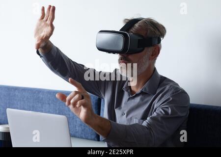 Caucasian businessman sitting using vr googles and laptop in modern office Stock Photo