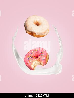 Two donuts doughnuts falling into a splash of milk on a pink background with copy space and room for text. Stock Photo