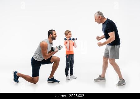 happy man demonstrating strength while father and son exercising with dumbbells on white Stock Photo