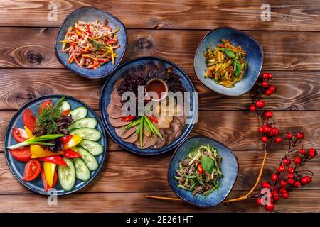 Flat layout of various dishes with sliced vegetables, meat cuts, salads on a brown wooden background. Stock Photo