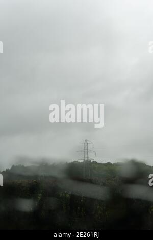 Looking through a car window blurred by raindrops, at an electricity pylon. On a bleak, rainy day. Stock Photo