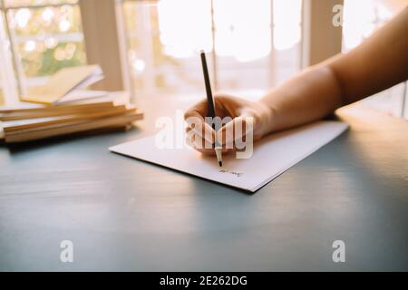 woman writing letters on gray desk with white papers and black pen. corona virus and quarantine. new hobbies. spend time at home. pen friend. front of Stock Photo