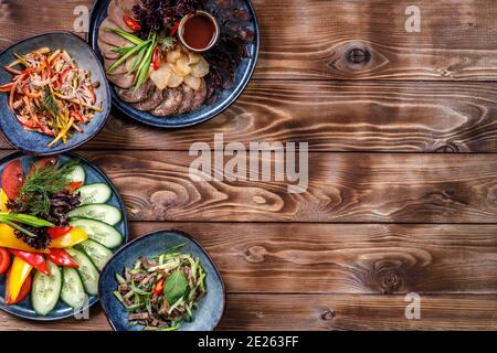 Flat layout of various dishes with sliced vegetables, meat cuts, salads on a brown wooden background. Copy space. Stock Photo