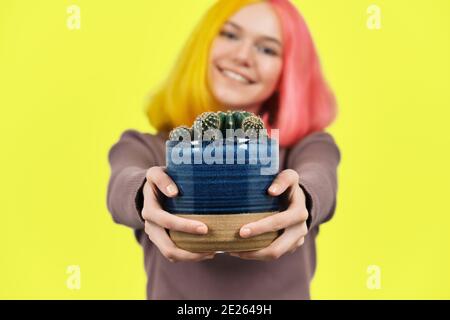 Smiling fashionable teenager girl with cactus plant in pot on yellow background Stock Photo
