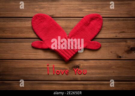 Valentines day card with heart made of red mittens on wooden vintage background and phrase about love Stock Photo