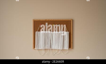 Surgical and medical masks hanging on colorful pins on a wooden framed cork board in white background. coronavirus pandemic lockdown 2021 Stock Photo