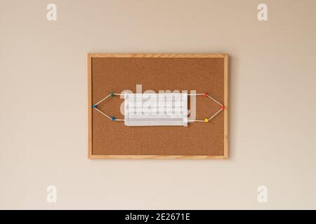 Surgical and medical masks hanging on colorful pins on a wooden framed cork board in white background. coronavirus pandemic lockdown 2021, self-care, Stock Photo