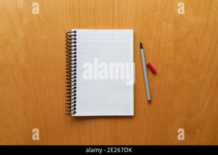 white notebook and red pencil on wooden table background, graph, grid black squared, isolated. blank paper. taking note. new year's resolution, goals. Stock Photo