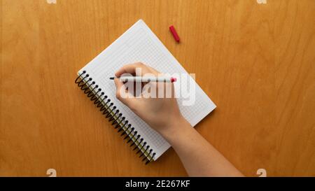 Taking notes in blank paper white notebook. graph, grid, black squared, woman hand and red pencil on wooden table background. new year's resolution, g Stock Photo