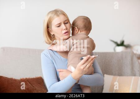 Concerned young mother looking at thermometer, kid got sick Stock Photo