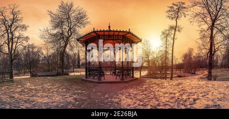 Panoramic view of sunset over metal openwork gazebo in public park in winter Stock Photo