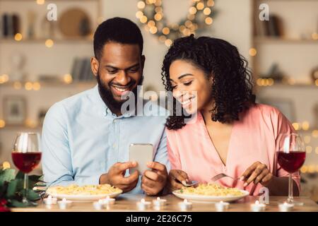 Smiling black man and woman using mobile phone during dinner Stock Photo
