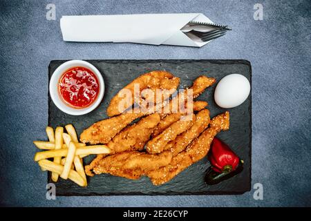 Chicken nuggets on the plate with fries served on the table with knife and fork Stock Photo