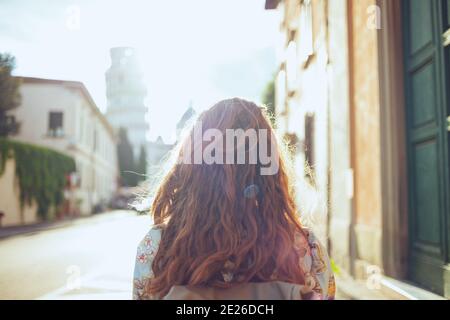 Seen from behind middle aged traveller woman in floral dress with backpack sightseeing in Pisa, Italy. Stock Photo