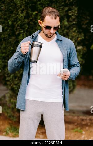 Man in white t-shirt using phone and drinks coffee mockup Stock Photo