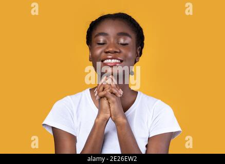 African American Woman Praying Standing On Yellow Studio Background Stock Photo