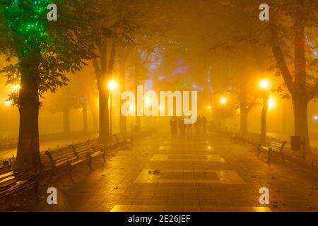 People walking at Odessa city center park alley in the heavy night fog. Odessa, Ukraine Stock Photo