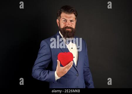 Trust me. Happy valentines day. Tuxedo man hold red heart. Love concept. Passionate mature lover hipster in formal suit. Businessman with bow tie. Romantic greeting. Fall in love. Celebrate love. Stock Photo