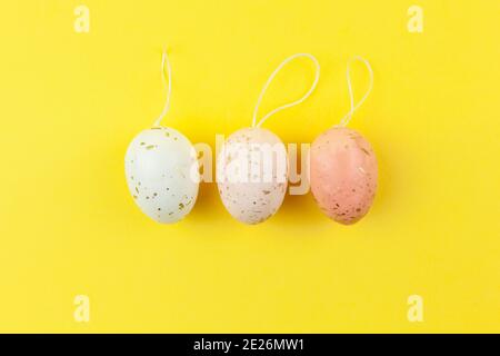 Three creatively painted eggs in pastel colors decorated with gold leaf are arranged in row on illuminating yellow background, copy space. Happy Easte Stock Photo
